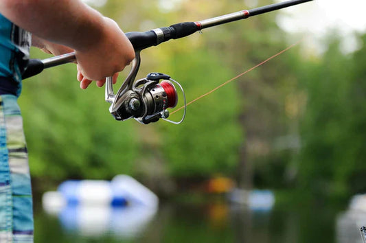 Close-up of person fishing with a spinning reel rod near a calm lake